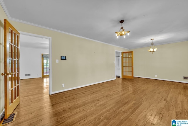 spare room featuring a notable chandelier, light hardwood / wood-style floors, ornamental molding, and french doors