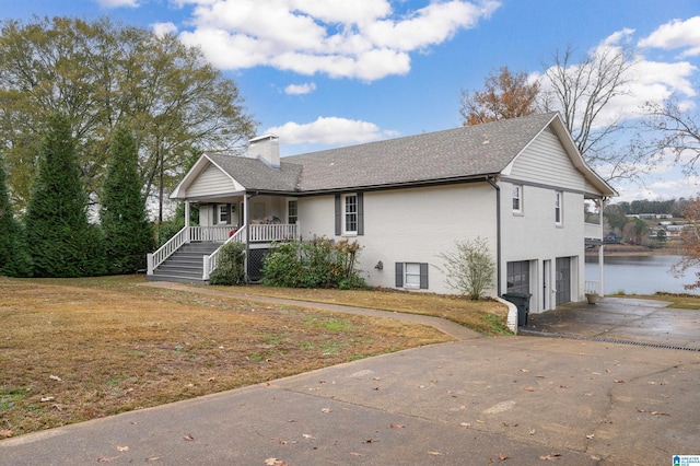 view of front of home with covered porch, a garage, a water view, and a front lawn