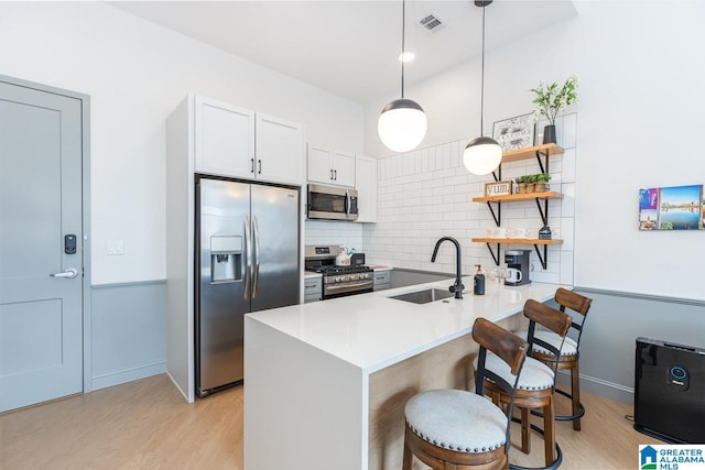 kitchen with a kitchen breakfast bar, kitchen peninsula, sink, appliances with stainless steel finishes, and white cabinetry