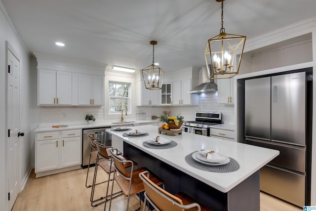 kitchen with white cabinets, light hardwood / wood-style floors, wall chimney range hood, and appliances with stainless steel finishes