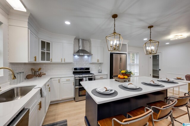 kitchen with wall chimney exhaust hood, hanging light fixtures, a kitchen bar, white cabinets, and appliances with stainless steel finishes