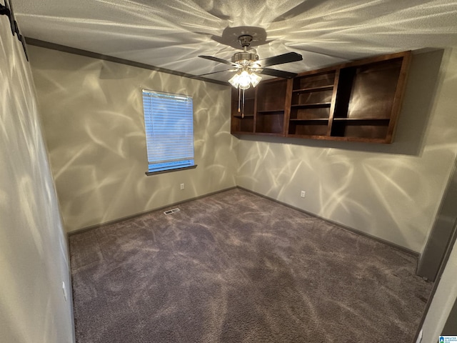 spare room with ceiling fan, a textured ceiling, and dark colored carpet