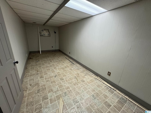 basement featuring a paneled ceiling and wood walls