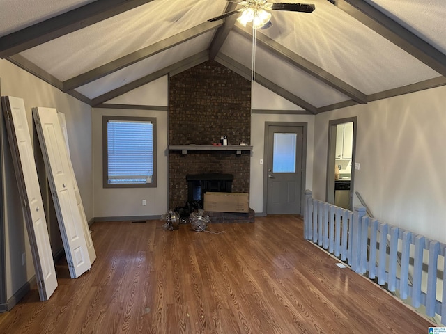 unfurnished living room featuring dark hardwood / wood-style flooring, lofted ceiling with beams, a brick fireplace, and ceiling fan