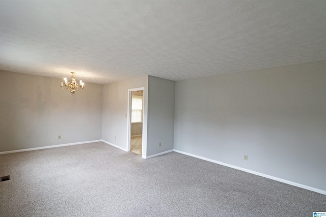 carpeted empty room featuring a chandelier and a textured ceiling