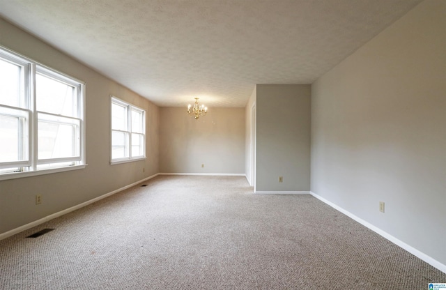 carpeted empty room with a textured ceiling and a notable chandelier