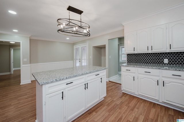 kitchen with light wood-type flooring, ornamental molding, pendant lighting, white cabinets, and a kitchen island