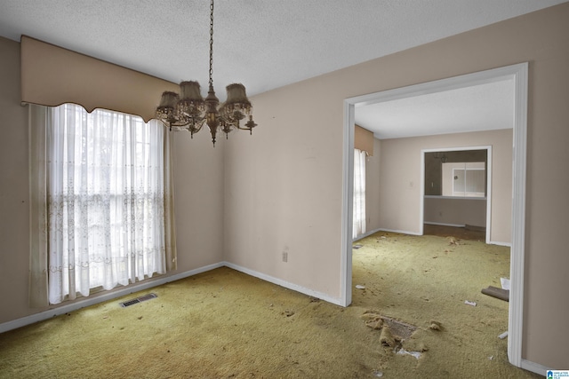 unfurnished dining area with a healthy amount of sunlight, a textured ceiling, and an inviting chandelier