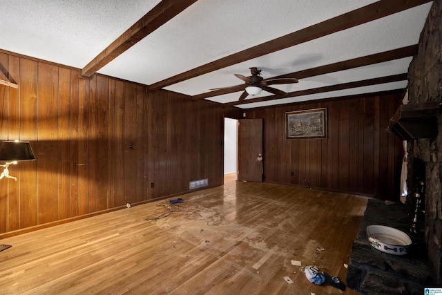 unfurnished living room featuring hardwood / wood-style flooring, ceiling fan, wood walls, and beamed ceiling