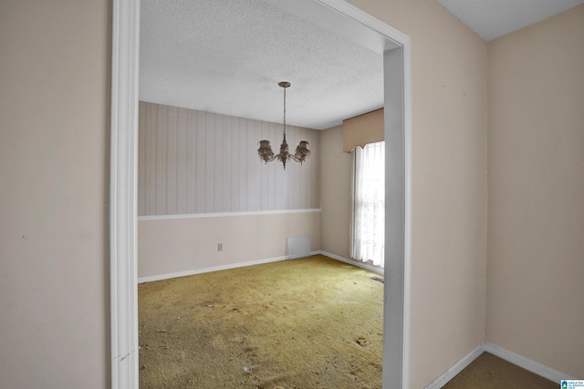 carpeted spare room with a textured ceiling and a notable chandelier