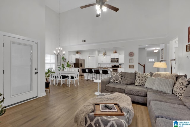 living room with high vaulted ceiling, ceiling fan with notable chandelier, and light wood-type flooring