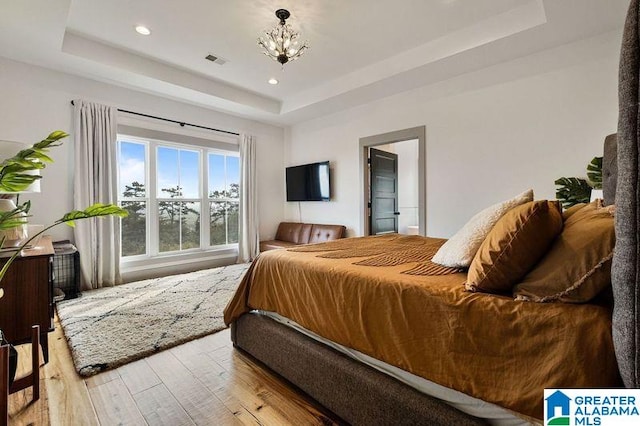 bedroom with a tray ceiling, light hardwood / wood-style floors, and a notable chandelier