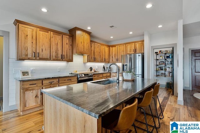 kitchen featuring a kitchen island with sink, sink, light hardwood / wood-style flooring, a breakfast bar area, and stainless steel appliances