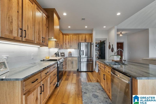 kitchen with dark stone counters, sink, ceiling fan, light wood-type flooring, and stainless steel appliances