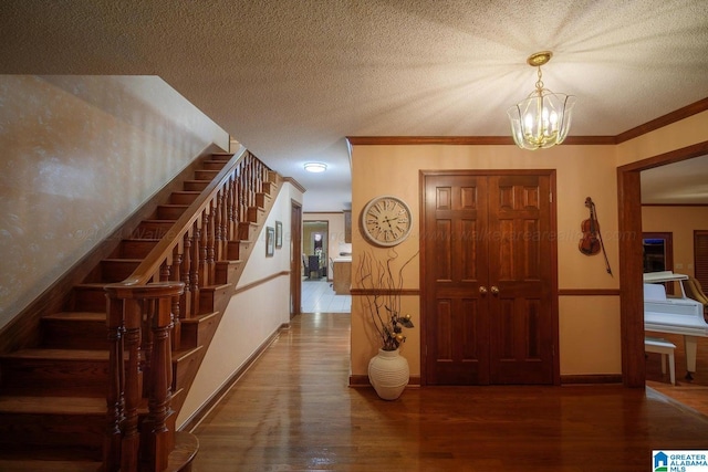 foyer entrance with a chandelier, wood-type flooring, a textured ceiling, and ornamental molding