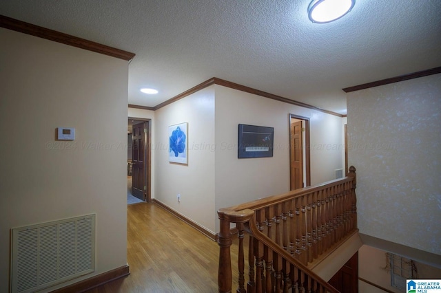 corridor with a textured ceiling, light wood-type flooring, and ornamental molding