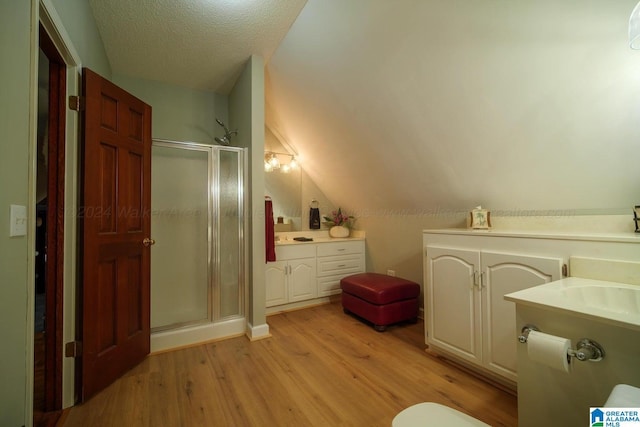 bathroom with walk in shower, a textured ceiling, lofted ceiling, vanity, and hardwood / wood-style flooring