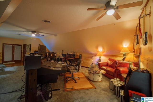 carpeted home office featuring ceiling fan, lofted ceiling, and wood walls