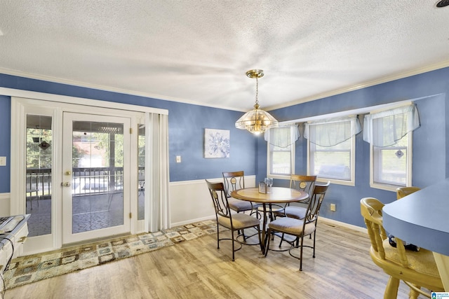 dining space featuring a textured ceiling, light wood-type flooring, ornamental molding, and a notable chandelier