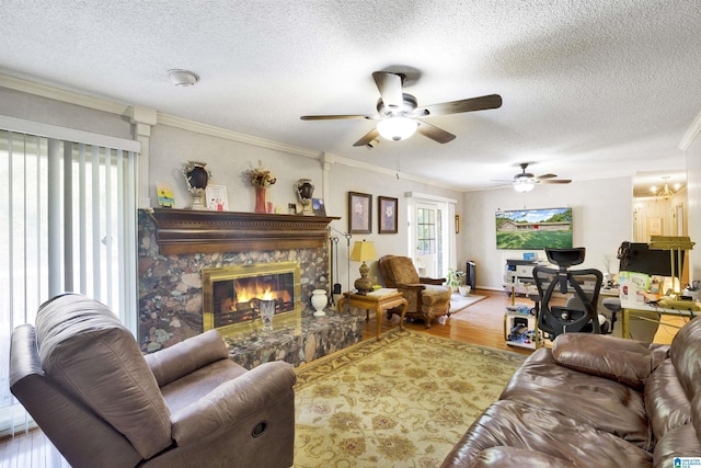 living room with ceiling fan, crown molding, a textured ceiling, a fireplace, and hardwood / wood-style flooring