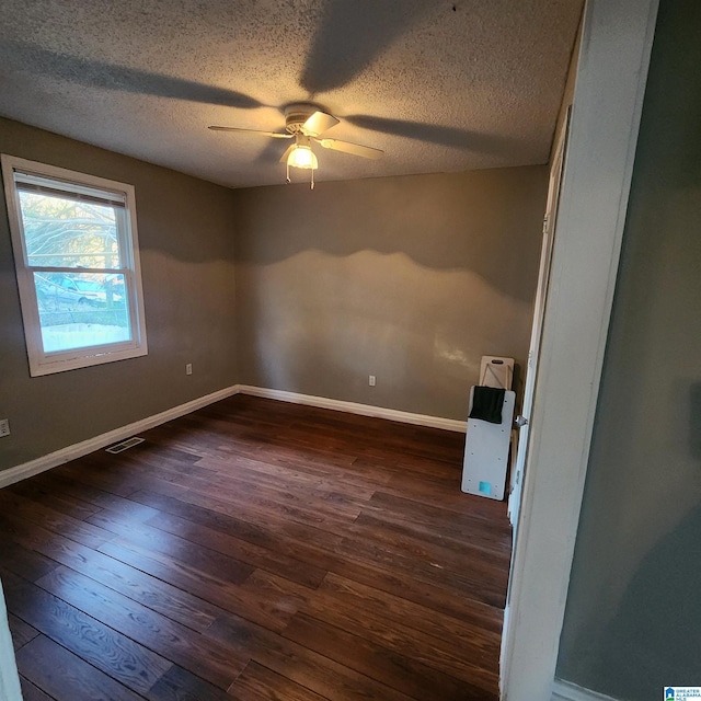 empty room with ceiling fan, dark wood-type flooring, and a textured ceiling