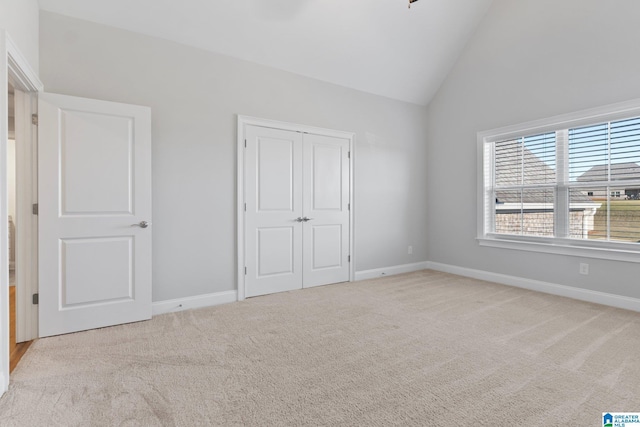 unfurnished bedroom featuring light carpet, a closet, and high vaulted ceiling