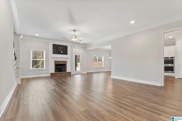 unfurnished living room featuring light wood-type flooring, a brick fireplace, ceiling fan, and crown molding