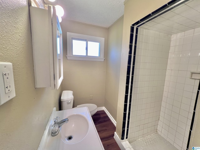 bathroom with sink, toilet, a textured ceiling, tiled shower, and wood-type flooring