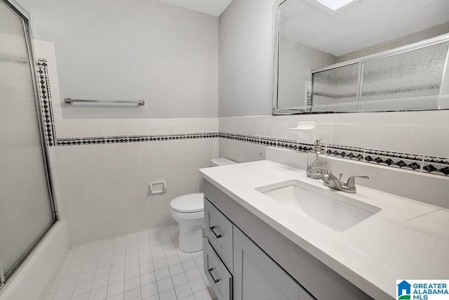 full bathroom with tile patterned flooring, enclosed tub / shower combo, toilet, vanity, and tile walls