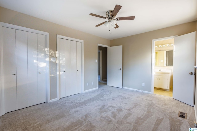 unfurnished bedroom featuring light carpet, two closets, ensuite bath, and ceiling fan