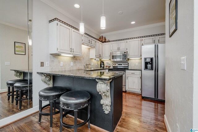 kitchen with white cabinets, crown molding, dark hardwood / wood-style floors, appliances with stainless steel finishes, and a kitchen bar