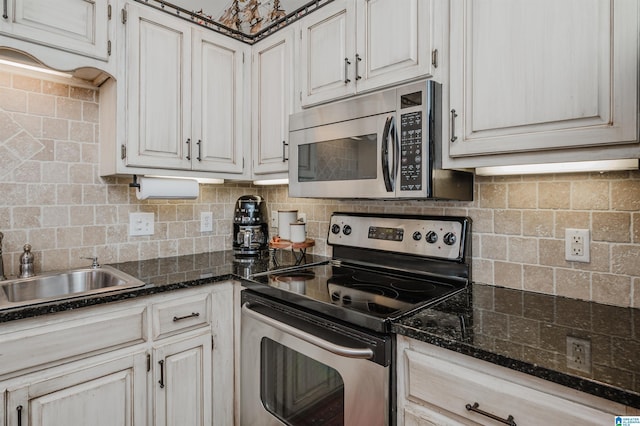 kitchen with dark stone counters, white cabinets, sink, tasteful backsplash, and stainless steel appliances