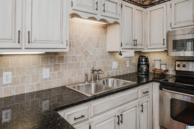 kitchen featuring decorative backsplash, stainless steel appliances, sink, dark stone countertops, and white cabinetry