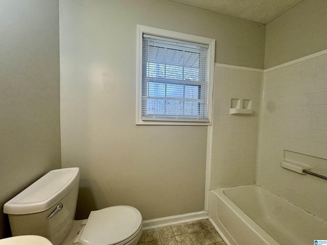 bathroom featuring washtub / shower combination, tile patterned floors, a textured ceiling, and toilet