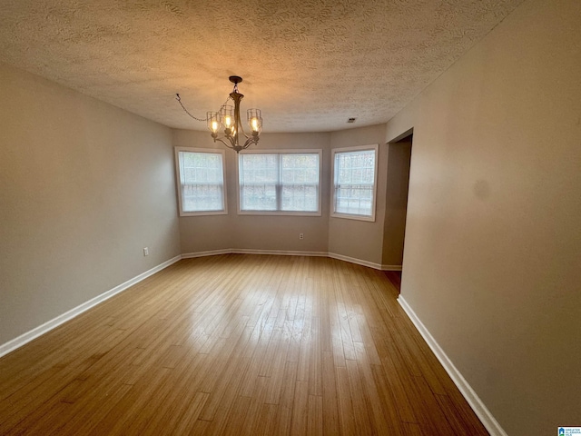 unfurnished room featuring a chandelier, wood-type flooring, and a textured ceiling