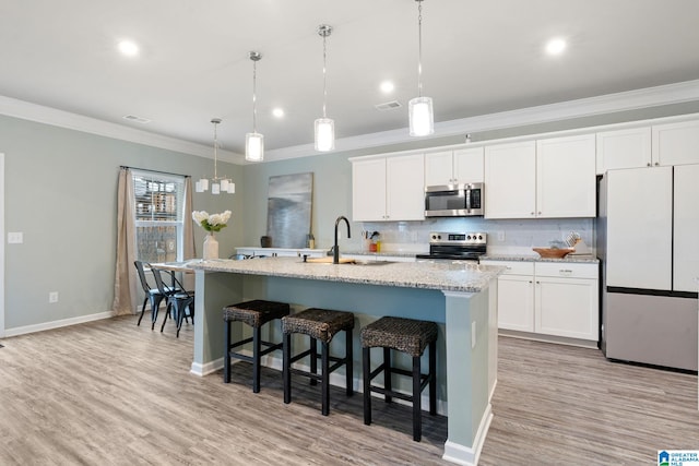 kitchen with a center island with sink, sink, hanging light fixtures, white cabinetry, and stainless steel appliances