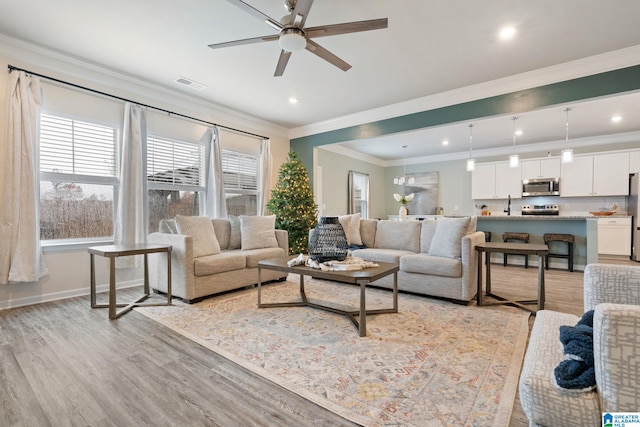 living room with ceiling fan with notable chandelier, light hardwood / wood-style floors, and crown molding