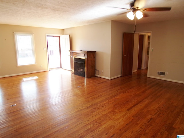 unfurnished living room featuring hardwood / wood-style flooring, ceiling fan, and a textured ceiling