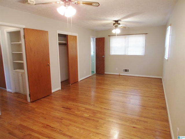 unfurnished bedroom with a textured ceiling, ceiling fan, light hardwood / wood-style floors, and two closets