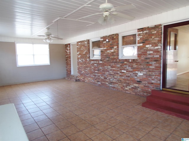 spare room with ceiling fan and brick wall