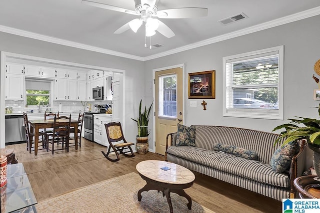 living room with crown molding, light hardwood / wood-style flooring, ceiling fan, and sink