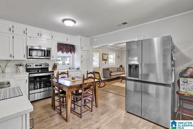 kitchen with white cabinets, ornamental molding, tasteful backsplash, light hardwood / wood-style floors, and stainless steel appliances