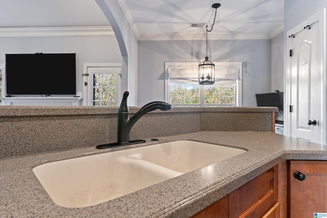 interior details with light stone counters, ornamental molding, sink, an inviting chandelier, and hanging light fixtures