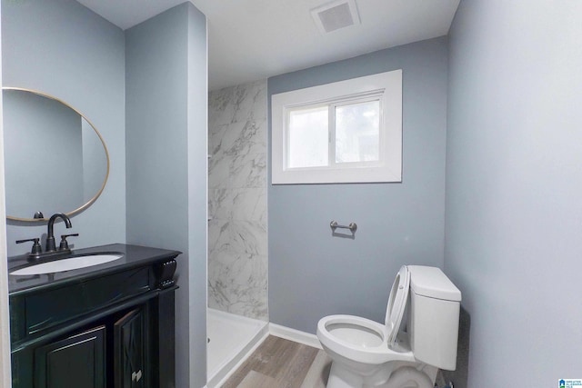 bathroom with hardwood / wood-style floors, vanity, a tile shower, and toilet