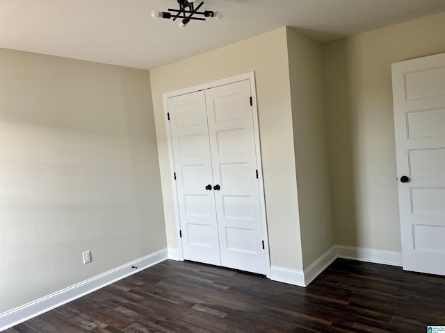 unfurnished bedroom featuring dark hardwood / wood-style floors, an inviting chandelier, and a closet