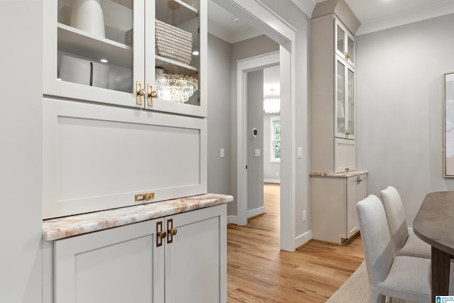 bar with white cabinets, light wood-type flooring, light stone countertops, and crown molding