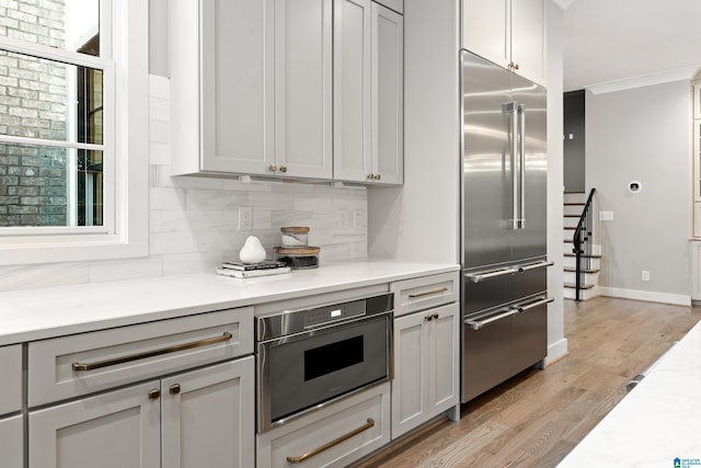 kitchen with decorative backsplash, light hardwood / wood-style floors, built in refrigerator, and gray cabinetry