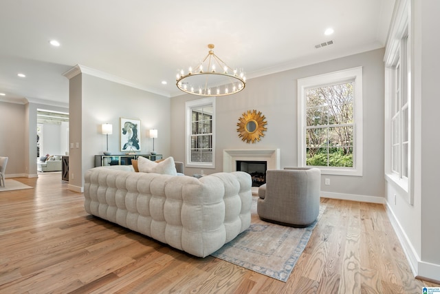 living room with light wood-type flooring, ornamental molding, and a notable chandelier