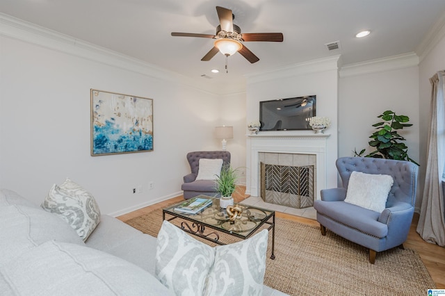 living room featuring a fireplace, hardwood / wood-style flooring, ceiling fan, and crown molding