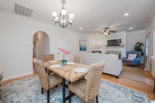 dining room with a tile fireplace, light hardwood / wood-style flooring, ceiling fan with notable chandelier, and ornamental molding